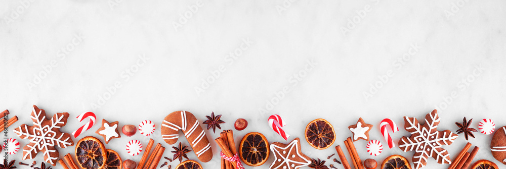 Poster christmas baking bottom border with cookies, peppermints and spices. top view over a white marble ba
