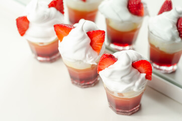 Colorful layered shots of drinks based on vodka, grenadine and orange juice decorated with whipped cream and pieces of strawberry in the shape of bunny ears