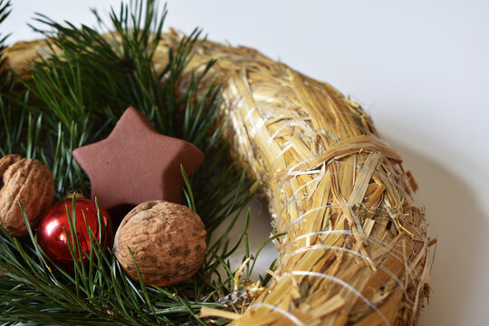 strohkranz mit N&uuml;ssen, Christbaumkugel in Rot, Reisig in Gr&uuml;n und Keramikstern in Braun vor Wei&szlig;em Hintergrund f&uuml;r Weichnachten, Advent, Deko f&uuml;r Weihnachtsfest