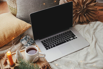 Laptop on soft bed, cup of tea, christmas lights, stars, pine, candle. Freelance, blog. Winter hygge