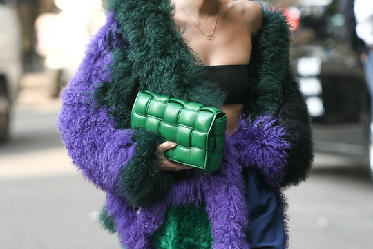 Milan, Italy - September 23, 2021:  Street style outfit, fashionable woman wearing a cropped t-shirt, a green shiny leather Cassette handbag from Bottega Veneta and an oversized fluffy coat.