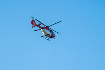 Red white helicopter flying in clear blue sky