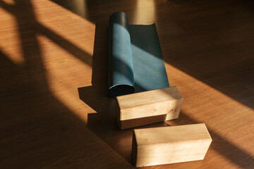 Closeup of two wooden yoga blocks and blue yoga mat on the wooden floor.