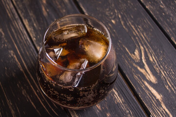 Beautiful glass with whiskey cola and ice on a dark brown wooden table background. Delicious and elegant gossed alcoholic cocktail at the bar.