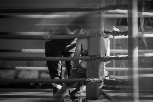 The corner of the boxing ring. The boxer rests between rounds. Retro style black and white background image with shallow depth of field. Sharpness on the athlete in the corner of the ring.