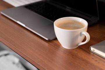 Fototapeta na wymiar A white cup of coffee next to a laptop