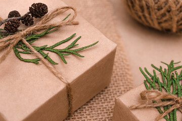 Festive decoration of gifts in eco-style.Gift boxes are wrapped in craft paper,tied with cotton thread,decorated with thuja leaves,cones and burlap,closeup.Christmas,New Year and eco-friendly concept.