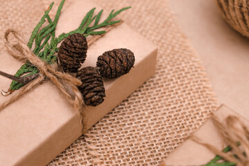 Festive decoration of gifts in eco-style.Gift boxes are wrapped in craft paper,tied with cotton thread,decorated with thuja leaves,cones and burlap,closeup.Christmas,New Year and eco-friendly concept.