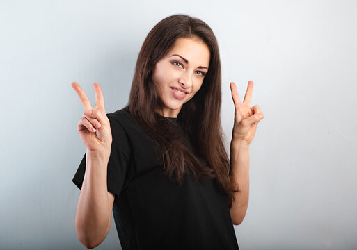 Pretty smiling excited woman with brunette long hair in casual black t-shirt looking happy. and showing victory signs by two hands. Studio shot of good looking woman