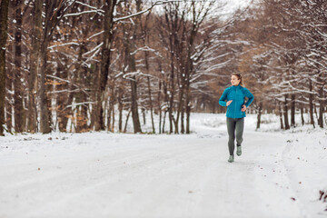 Fototapeta na wymiar Slim sportswoman jogging in nature on a snowy weather. Cold weather, snow, healthy life, fitness, healthy habits