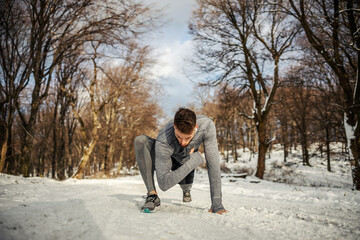 Fototapeta premium Fit sportsman doing warm up and stretching exercises while kneeling in nature at snowy winter day. Winter fitness, healthy lifestyle