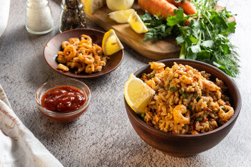 Freshly prepared dish. Paella with shrimp and lemon. Vegetables and herbs on the board.