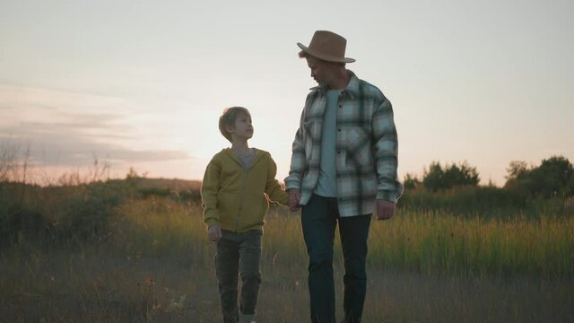 Caucasian bearded adult father with his cute son walking on wheat field, talking and smiling having great time outdoors. Affectionate family. Happy moments.