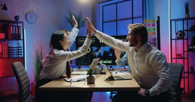 Office goals concept where attractive smiling confident experienced young diverse office workers giving high five each other during meeting in evening workroom