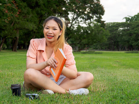 Portrait Young Asian Woman Long Hair Student Wearing Pink Shirt White Pants White Shoes Sitting Reading Book With Cup Coffee And Camera On Green Grass In Park Comfortably On Vacation Review Knowledge
