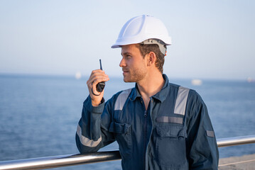 Workman talking on walkie talkie near sea