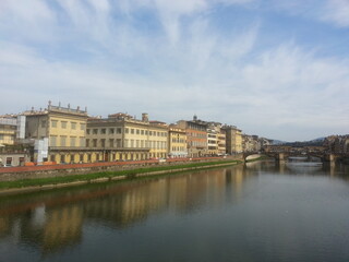 Fototapeta na wymiar Florence, la capitale de la Toscane, le fleuve Arno longeant la ville, ses maisons colorés en jaune ou orange, avec pont au fond, balade tranquille aquatique et communale, ciel nuageux