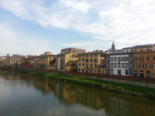 Fototapeta na wymiar Florence, la capitale de la Toscane, le fleuve Arno longeant la ville, ses maisons colorés en jaune ou orange, avec pont au fond, balade tranquille aquatique et communale, ciel nuageux