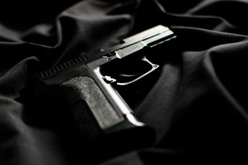 Black handgun, pistol on black fabric background, close up