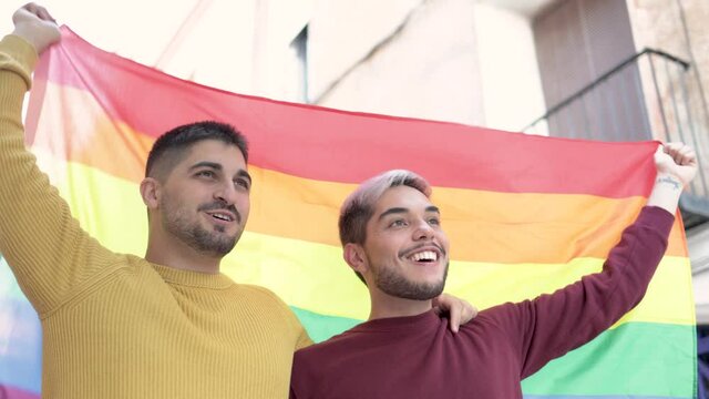 Gay male couple holding rainbow flag at Lgbt pride parade - Focus on right man face