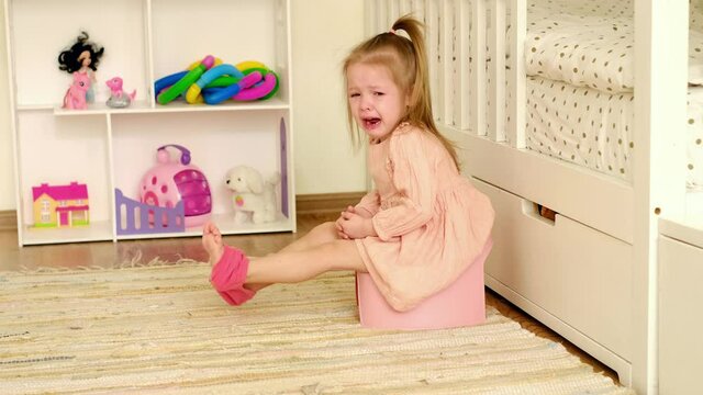 Baby sobs bitterly shedding tears while sitting on a potty in the children's room. Teaching a child to pee in the toilet on his own. Child psychology. Parenting and child care