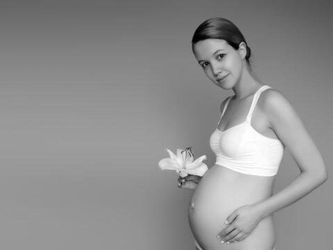 Beautiful pregnant young woman in clothes for pregnant women is measuring her bare tummy, smiling, on a biege background. Picture of happy pregnant woman posing over wall. Looking at camera