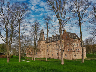 Fototapeta premium The medieval castle of Doorwerth on the river Rhine in the Netherlands, with green grass and large trees in the foreground. The castle was severely damaged in WW2, but has been restored 
