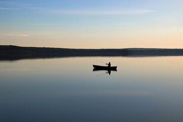 Obraz na płótnie Canvas Silhouette of a man fishing in a canoe on a still morning