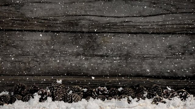 Animation of christmas snow falling over wooden boards and pine cones