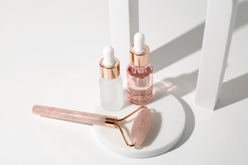 Massage quartz roller and two glass bottles of cosmetic liquid transparent gel on white background. Dropper bottle, hyaluronic acid, oil, serum. Facial massage and relaxation. Gua Sha massage tools.