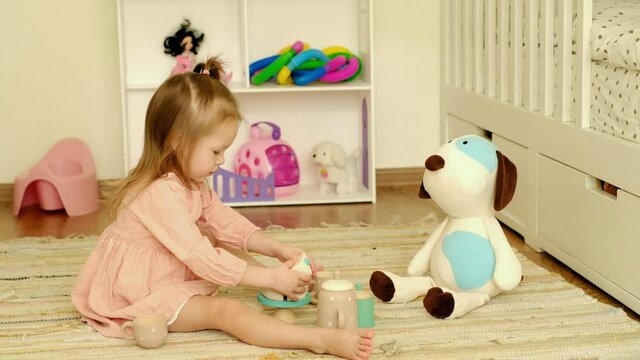 Kid collects a toy wooden cake from pieces on a stand. A girl is playing a tea party with her friend a stuffed puppy. Children's exciting games. A set of wooden dishes for toddlers