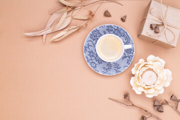 Top view for autumn composition. A cup of coffee, dry eucalyptus leaves, a gift wrapped in craft paper and a candle in the form of a flower on a beige background. Flat lay, copy space