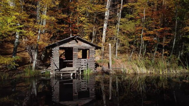 Fisherman's hut on the lake in the autumn forest. Bright foliage and smooth water surface. A cozy quiet place for meditation. The nature of the Crimea.