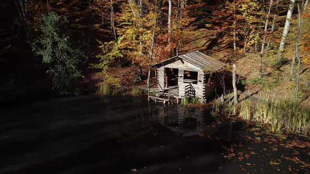 Fisherman's hut on the lake in the autumn forest. Bright foliage and smooth water surface. A cozy quiet place for meditation. The nature of the Crimea.