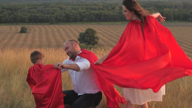 little child with mother and father playing superheroes dressed in red cloaks, happy family, brave savior costume, fantastic childhood dream heroes, fearless kid boy winner, fun to play the game