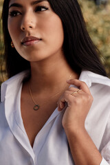 Latin woman with rings and pendant adjusting the collar of her white shirt. model with jewelry.
