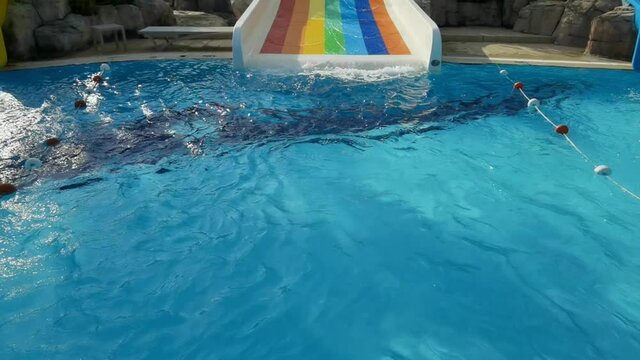 Water slowly flows down from children plastic multicolored slide into hotel empty pool.