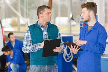 apprentice mechanic holding tablet in garage supervisor holding clipboard