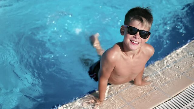 Relaxed male kid posing at swimming pool playing legs at bright water splash slow motion