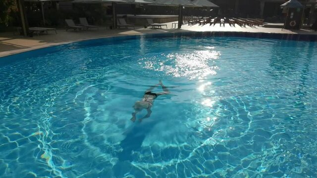 Active young woman diving in pool and splashing water. Lady relaxing on tropical resort. Woman in swimsuit jumping into basin with cool refreshing water at sunny day. Summer vacation concept