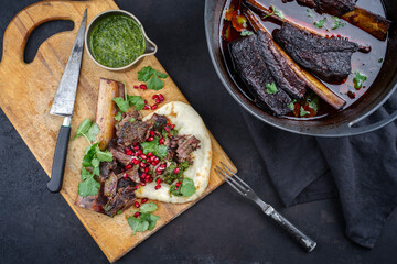 Traditional braised chuck beef ribs in red wine sauce and chimichurri served as top view in a...