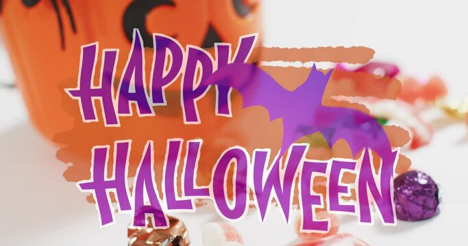 Happy halloween text banner with bat icon against pumpkin shaped bucket full of halloween candies