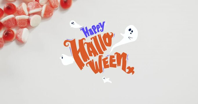 Happy halloween text banner and ghosts icons against close up of candy corns on white surface