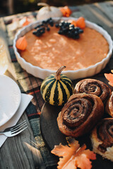 Thanksgiving festive table. Autumn style table setting with pumpkins, leaves and physalis. Pumpkin pie and cinnamon rolls. Cozy autumn scene. Flat lay. Fall styled composition.