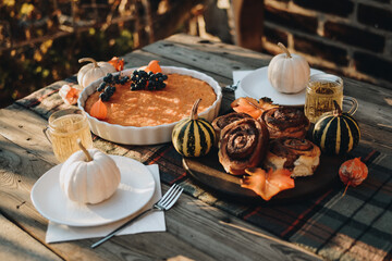 Thanksgiving festive table. Autumn style table setting with pumpkins, leaves and physalis. Pumpkin pie and cinnamon rolls. Cozy autumn scene. Flat lay. Fall styled composition.