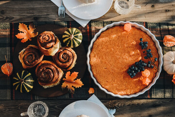 Obraz na płótnie Canvas Thanksgiving festive table. Autumn style table setting with pumpkins, leaves and physalis. Pumpkin pie and cinnamon rolls. Cozy autumn scene. Flat lay. Fall styled composition.