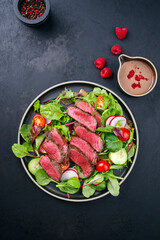 Fototapeta na wymiar Modern style traditional fried dry aged bison beef rump steak slices with vegetable, lettuce and mustard dressing served as top view on a Nordic design plate with copy space