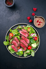 Modern style traditional fried dry aged bison beef rump steak slices with vegetable, lettuce and mustard dressing served as top view on a Nordic design plate with copy space