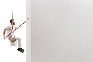 Side shot of a painter sitting on a swing and painting a wall with a paint roller