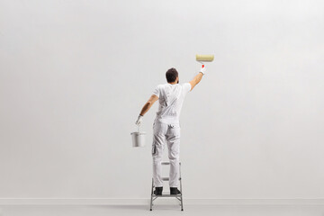 Rear view shot of a painter holding a bucket and painting a wall on a leader - Powered by Adobe